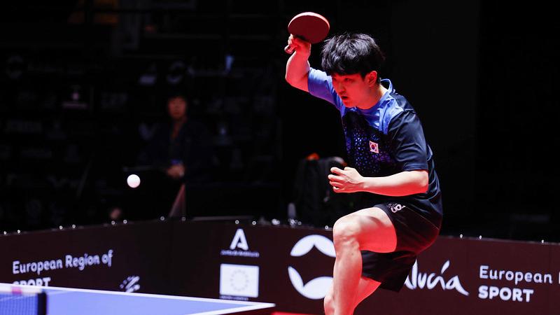 A male table tennis player jumps backward with a table tennis racket in his right hand