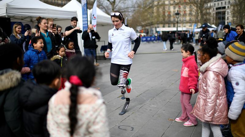 A woman with a prosthetic leg running in a square in the middle of a group of children and adults
