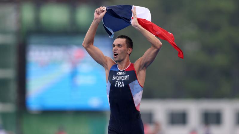 A male Para triathlete reacts to his victory at the Tokyo 2020 Paralympic Games by waving the French flag in the air.