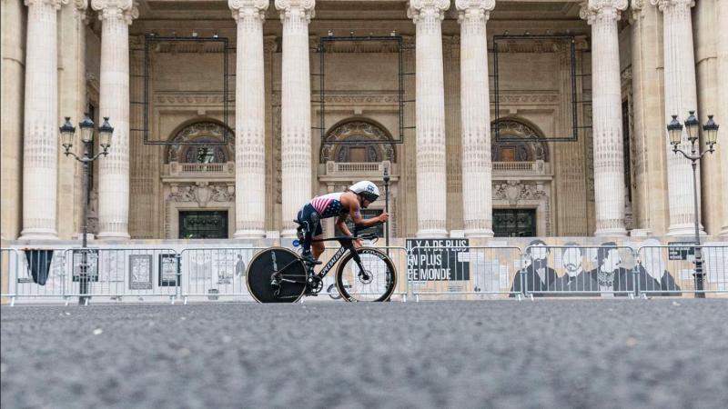 A Para triathlete on a bike cycles past a Parisian monument 