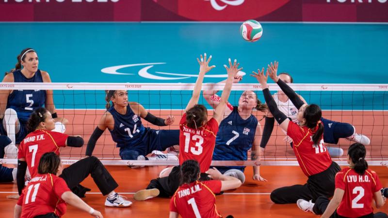 Two sitting volleyball athletes try to block the ball during a match.