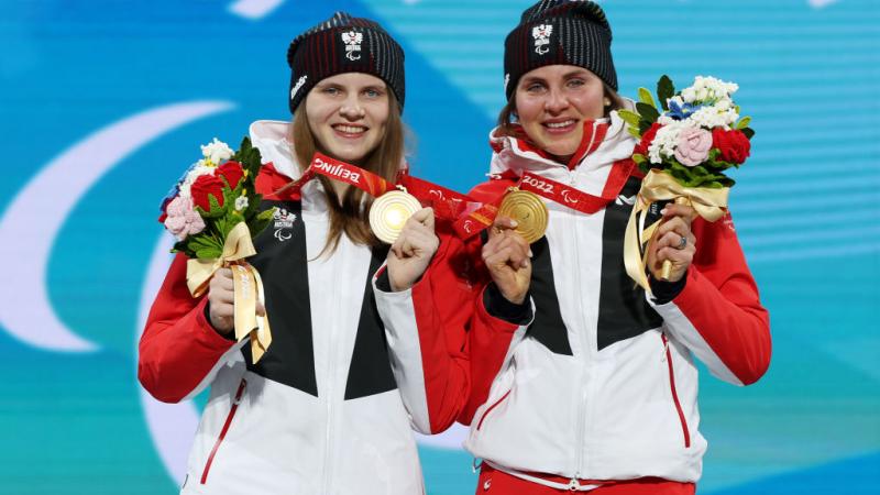 Two female athletes posing for a picture on the podium after receiving gold medals