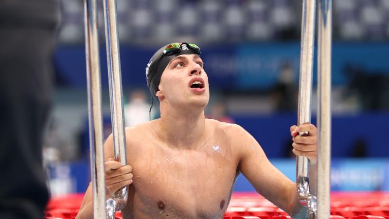 A male Para swimmer is using the handrails to leave the pool after a competition
