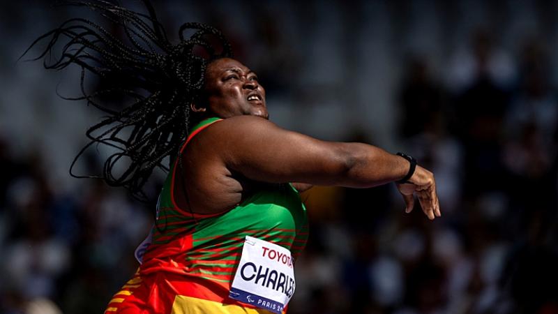 A female athlete wearing a red, yellow and green uniform is throwing