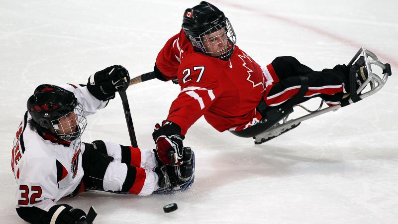 A picture of a 2 men in a sldege playing hockey