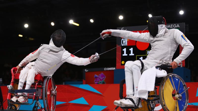 A picture of 2 men in wheelchairs fencing.