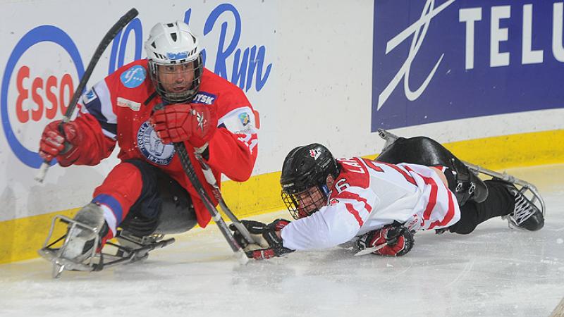 A picture of two men in a sledge playing ice sledge hockey.