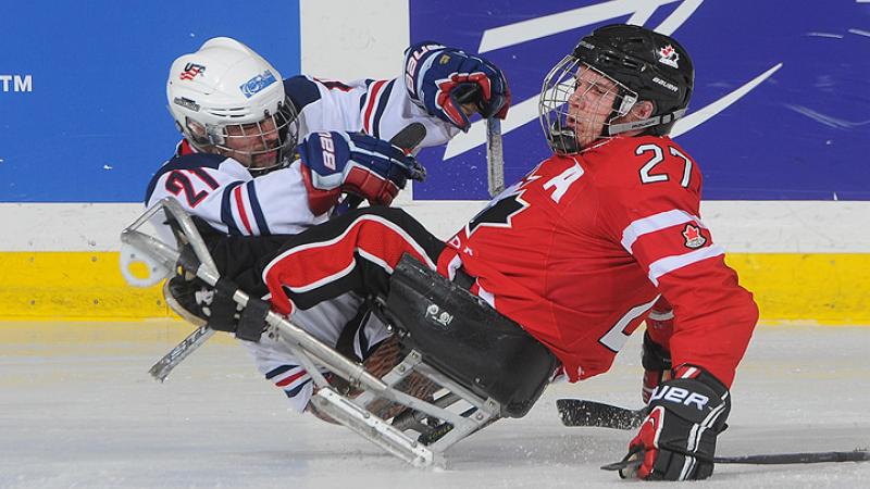 A picture of two men in sledges playing ice hockey