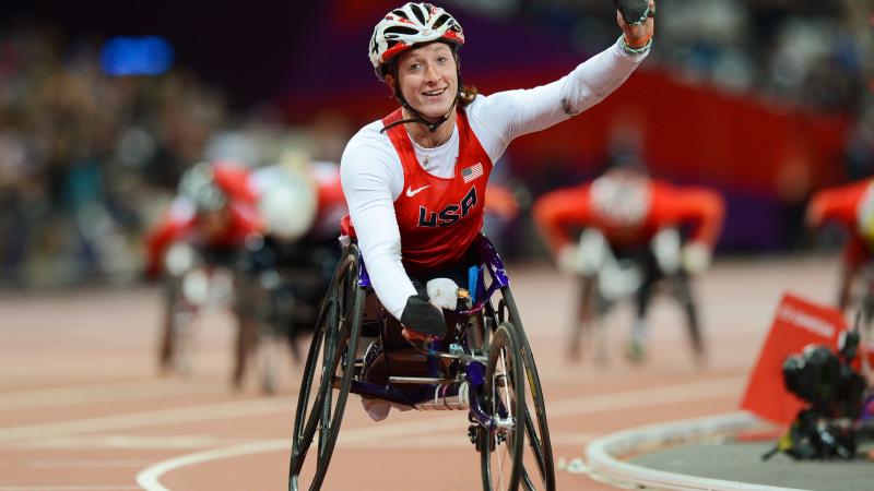 A picture of a woman in the wheelchair on a track celebrating with her hand up