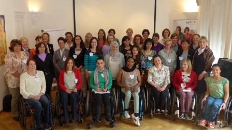 Group shot of women (standing and in wheelchairs) in front of a white wall.