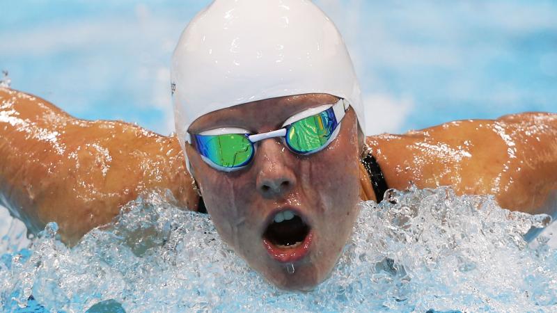 Women wearing swim goggles and a swim cap taking breath while swimming butterfly stroke.
