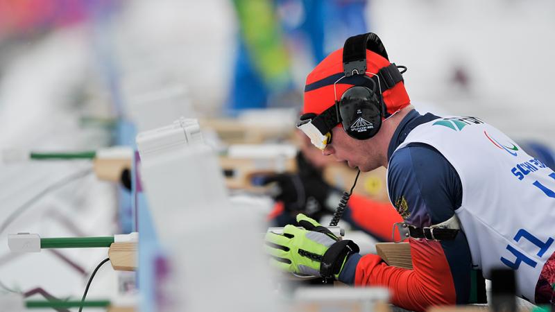 Athlete with ear phones takes aim in biathlon.