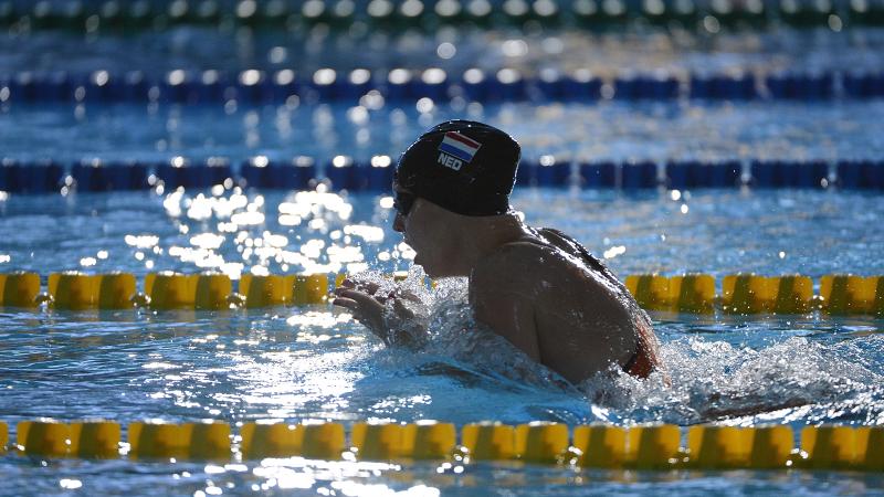 Women with black swim cap swimming breast stroke. Her head is out of the water as she is taking a breath