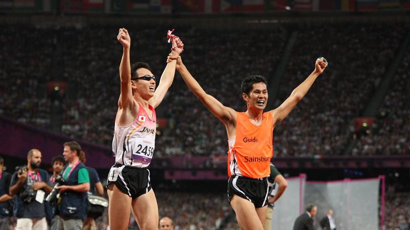 Runner with a guide crossing the finish line with their hands in the air