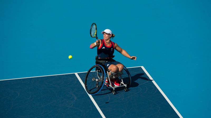 Woman in wheelchair playing tennis on a blue court