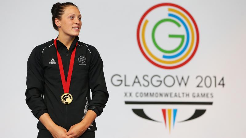 Women in training suit stand in front of a wall with the Glasgow 2014 logo