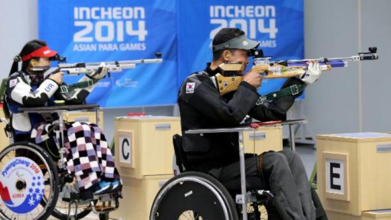 Two people in a shooting range, sitting in wheelchairs and targetting