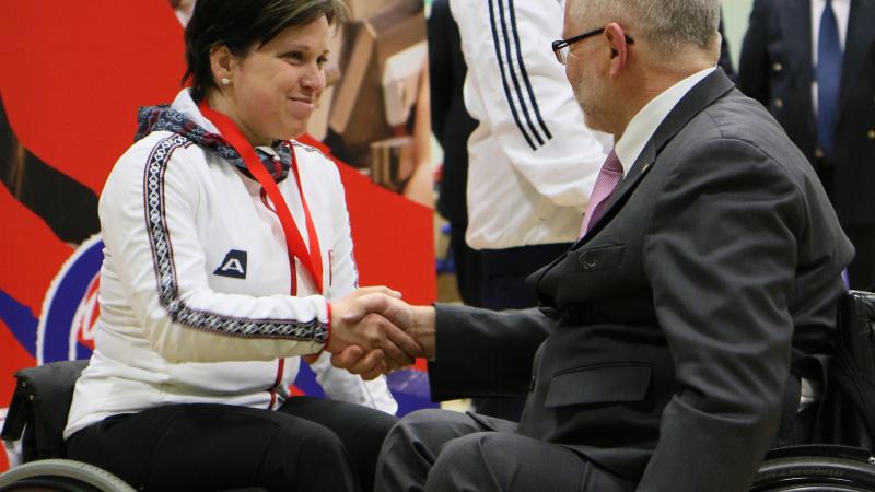 A female shooter in congratulated by a medal presenter