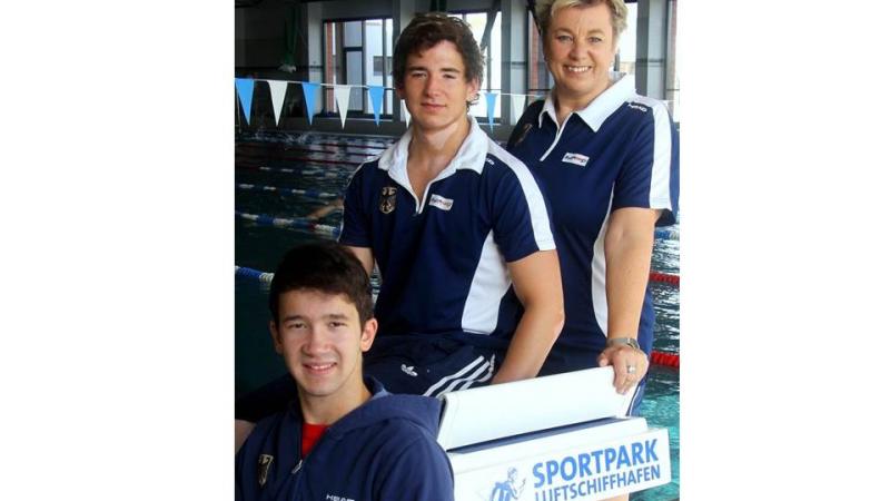 Two young boys and an adult woman pose in front of a swimming pool