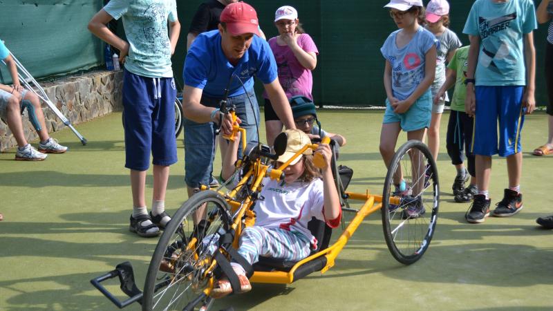 Kid in a handbike with other people standing around and watching