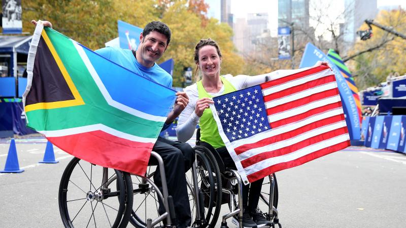 Man and woman in wheelchair hold their countries' respective flags.