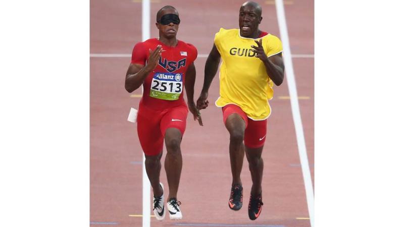 two men running, one with red clothes, one with a yellow t shirt saying guide
