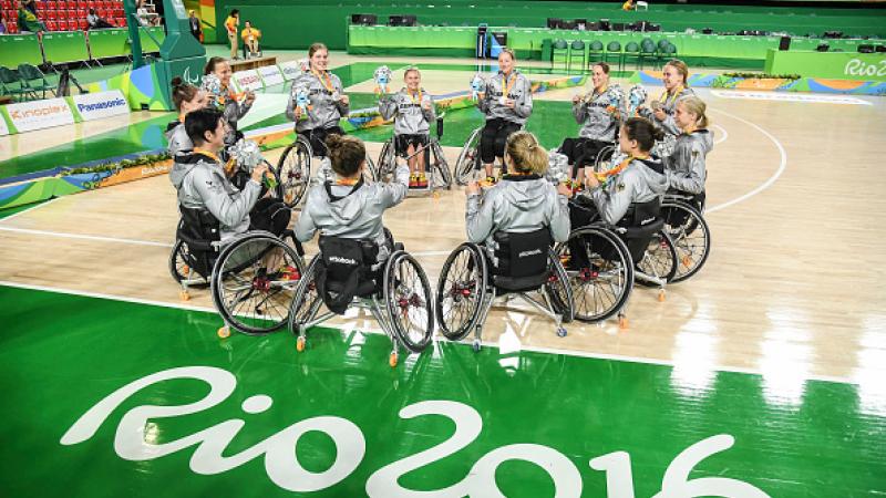 Women in wheelchairs forming a circle on a basketball field