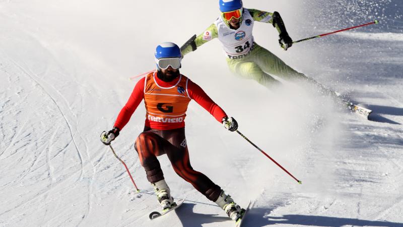 Vision impaired skier and his guide going down a slope