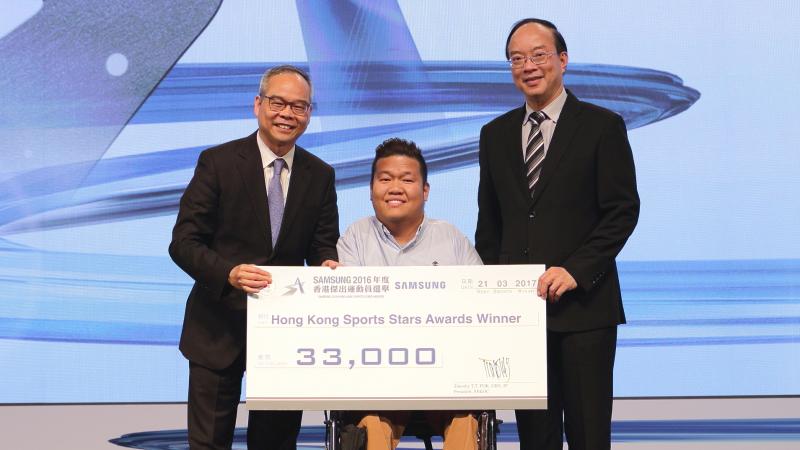 Man in middle in wheelchair holds giant check with two other men standing