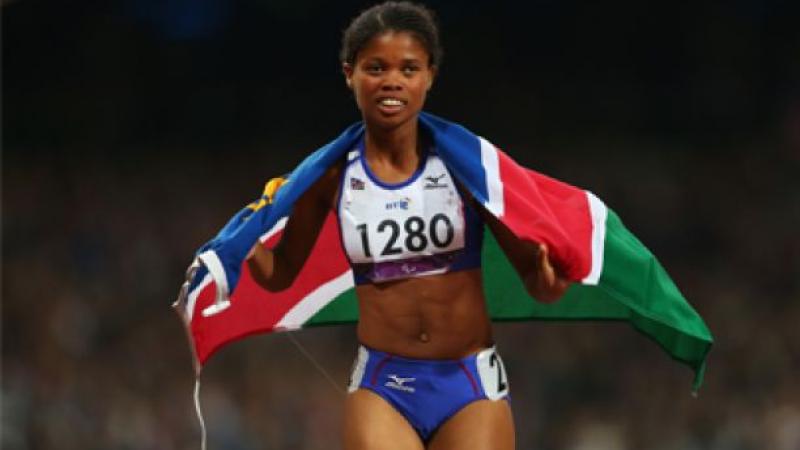 A picture of a woman running with a Namibian flag on her shoulder 