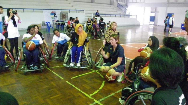 A coach kneels while women in wheelchairs gather around her 