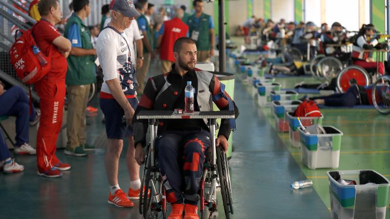 a para shooter in a wheelchair waits with his coach