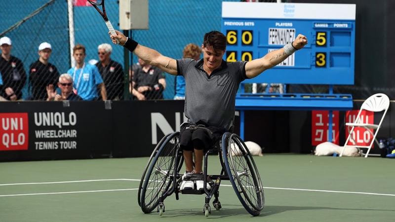 a wheelchair tennis player raises his arms in celebration
