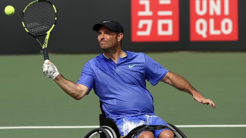 a male wheelchair tennis player hits a forehand