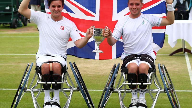 two male wheelchair tennis players hold their trophy and the British flag