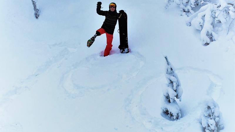 a male Para snowboarder stands on a '100' drawn in the snow