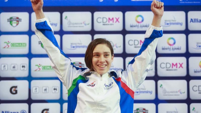 a female Para swimmer raises her arms on the podium