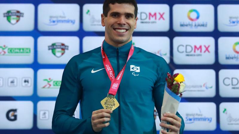 A male Para swimmer smiles holding his gold medal