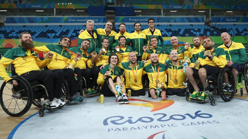 a group of wheelchair rugby players pose on the court with their medals