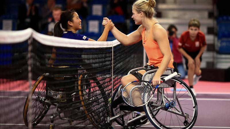 two female wheelchair tennis players shake hands over the net