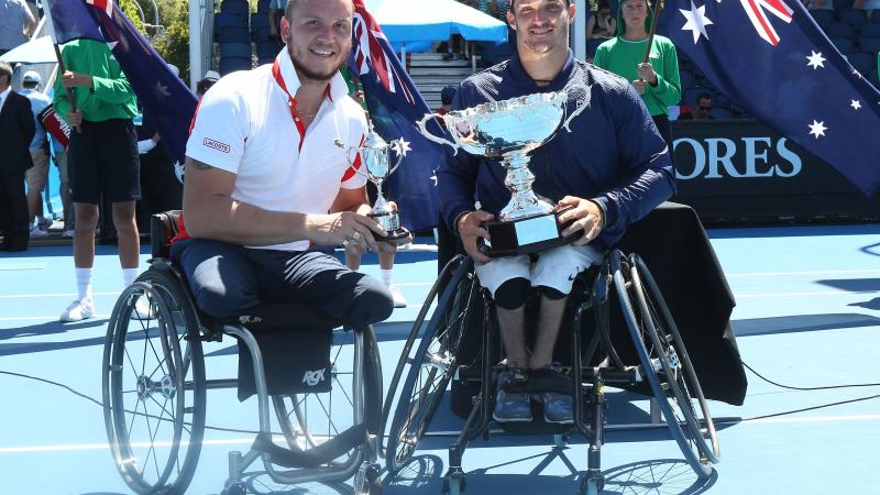 two male wheelchair tennis players hold up their trophies