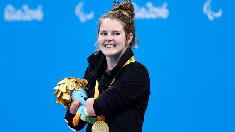 a Para swimmer smiles with her gold medal on the podium