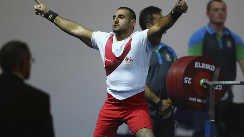 a male powerlifter raises his arms in celebration on the bench