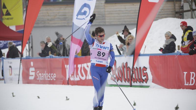 a male Para Nordic skier raises his arms in celebration as he crosses the finish line