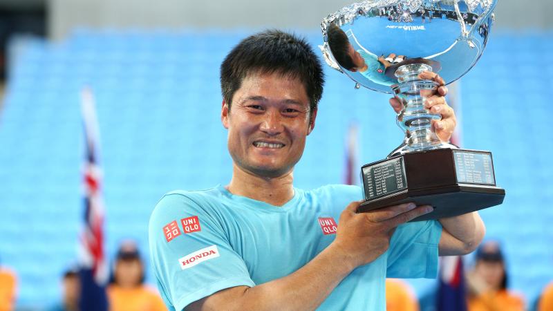 Man smiling and lifting a silver trophy