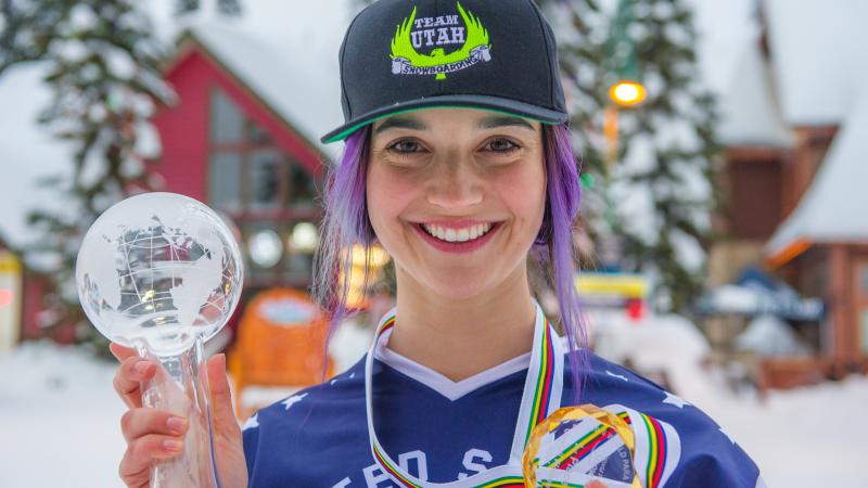 a female snowboarder holds up a crystal globe and medal