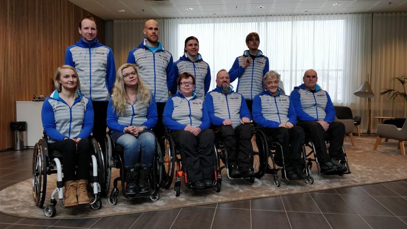 Four people standing behind a group of six people in wheelchairs