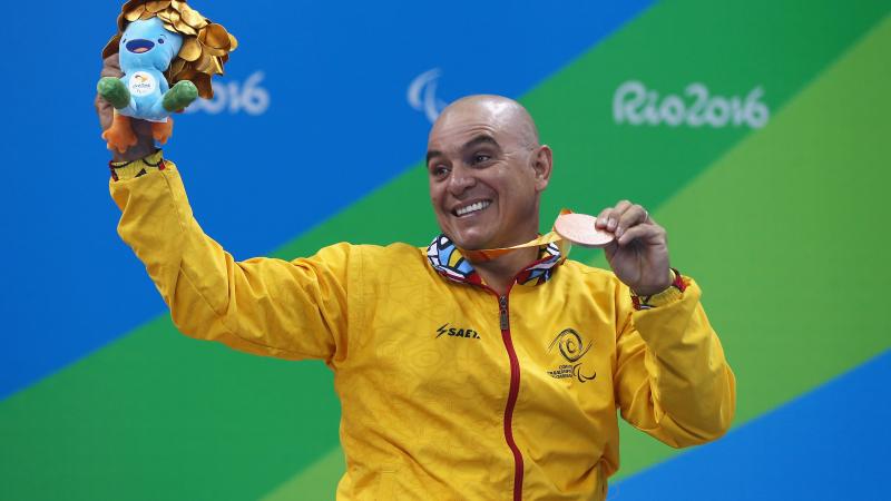a male Para swimmer holds his bronze medal aloft