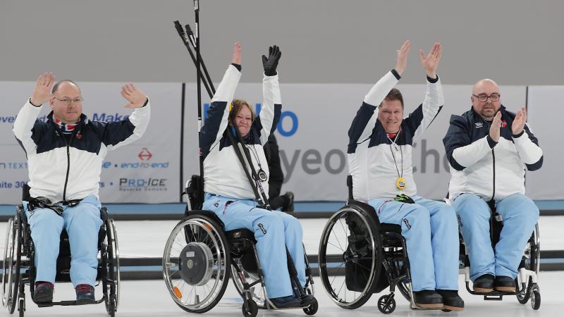 four wheelchair curlers raise their arms in celebration