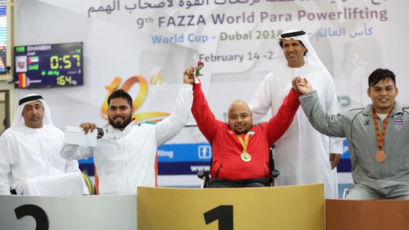 three male powerlifters raise their arms on the podium